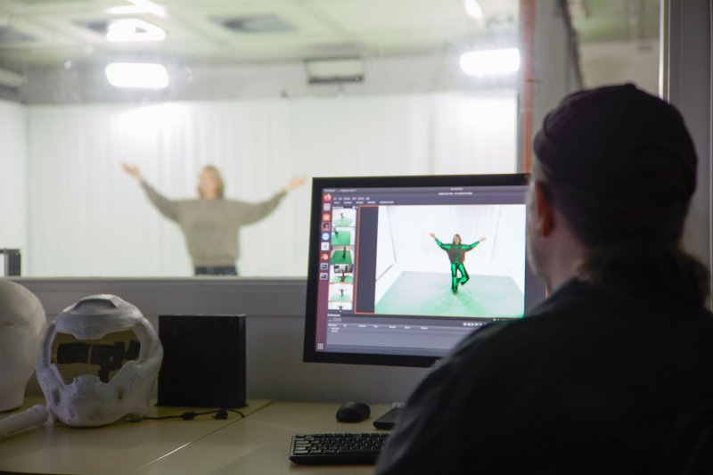 IM Hintergrund ist eine Studentin im Green Screen Labor zu erkennen, vorn sitzt jemand vor einem Bildschirm.