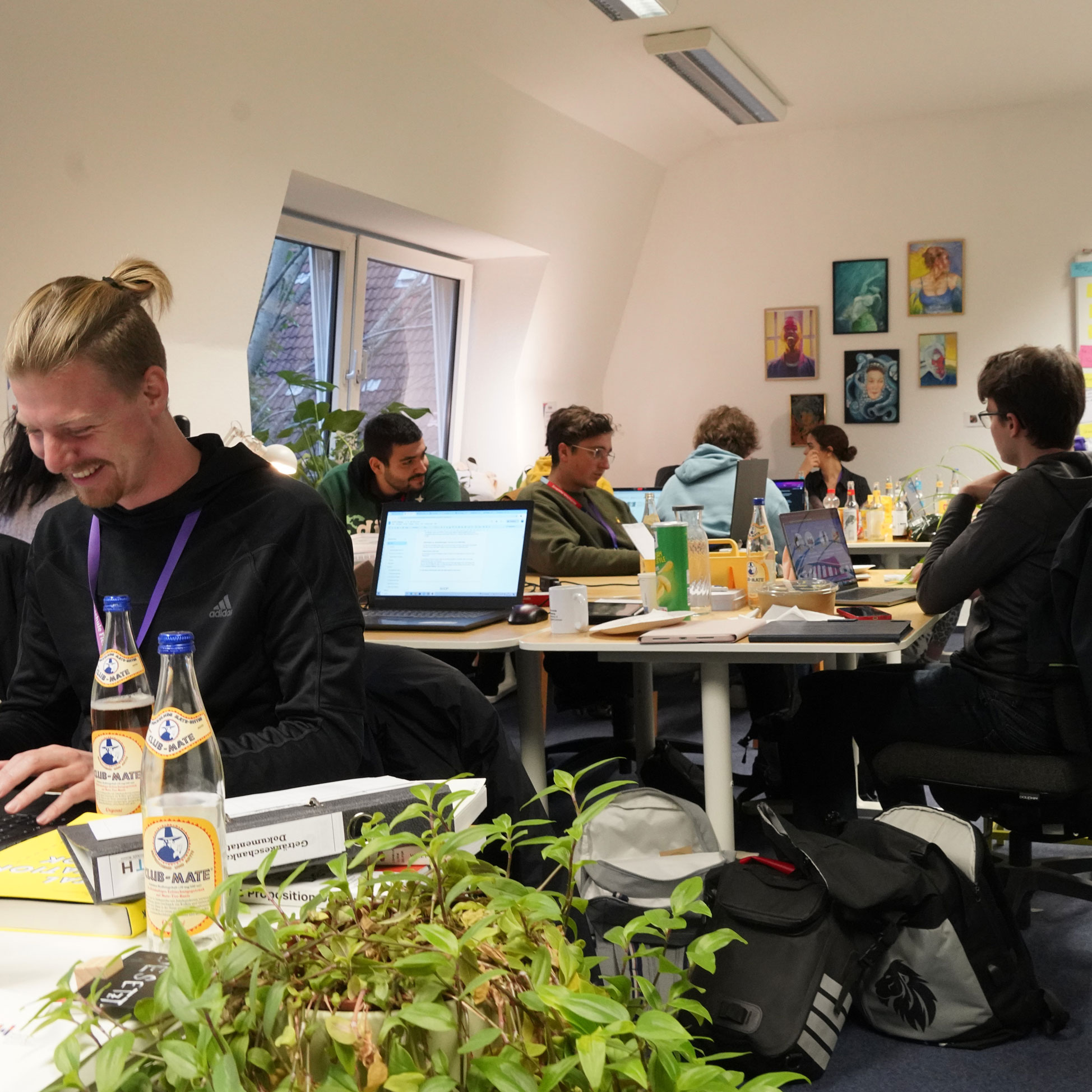 Menschen in einem Büroraum, sie sitzen an Tischen und arbeiten an Laptops.