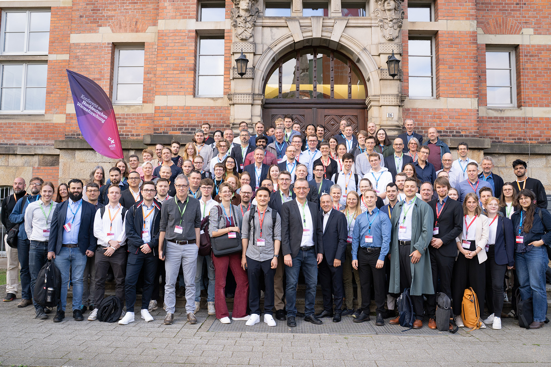 Gruppenfoto: Zahlreiche Menschen posieren vor dem Eingang eines Gebäudes. Alle tragen Lanyards mit Namensschildern.