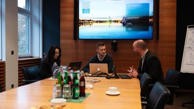 Drei Studierende sitzen an einem Tisch in einem Konferenzraum