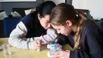 Zwei Mädchen sitzen an einem Tisch über ein Modellauto gebeugt. 