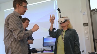 Eine Frau trägt eine VR Brille, ein Mann schaut zu 