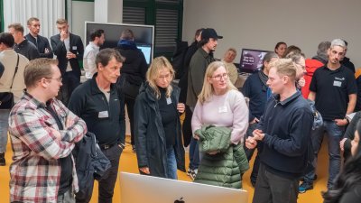 Viele Mensxchen stehen in einem Raum mit Computern und unterhalten sich. 