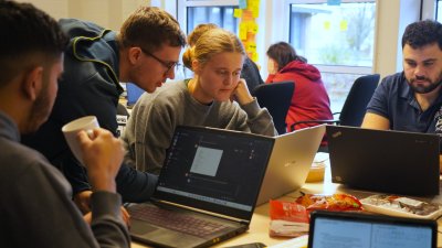 Viele Menschen stehen zusammen und schauen auf einen Laptop