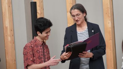 Eine Frau übergibt einem jungen Mann eine Urkunde