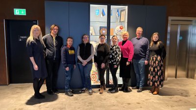 Eine Gruppe von Menschen steht in einem Foyer vor einer Vitrine mit estnischen Flagen und Kunst.