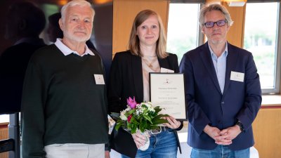Eine Frau steht mit Blumenstrauß zwischen zwei Männern