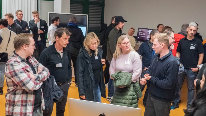 Viele Mensxchen stehen in einem Raum mit Computern und unterhalten sich.