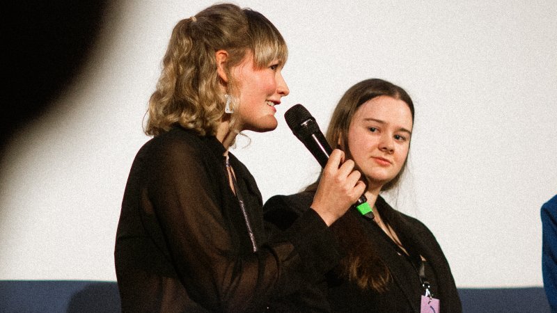 Zwei Frauen, eine spricht in ein Mikro, die andre schaut sie an