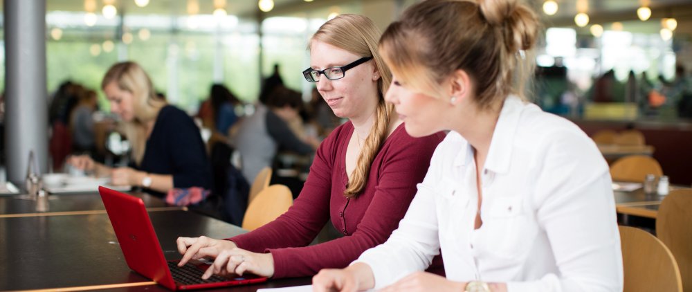 Zwei Studentinnen arbeiten in der Mensa am Laptop.