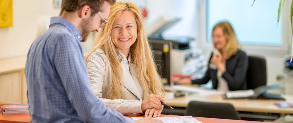 Eine Mitarbeiterin des Studierendenservice im Gespräch mit einem Studenten am Info-Point.