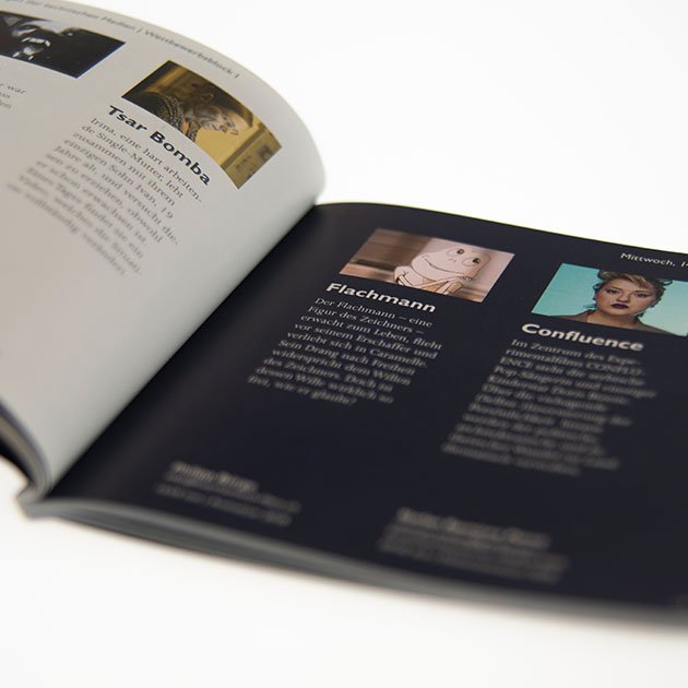 Ein aufgeblättertes Heft, wahrsceinlich ein Programmheft, in dem in mehreren Spalten nebeneinander Filme beschriben werden. Über jeder Spalte ist je ein Bild.