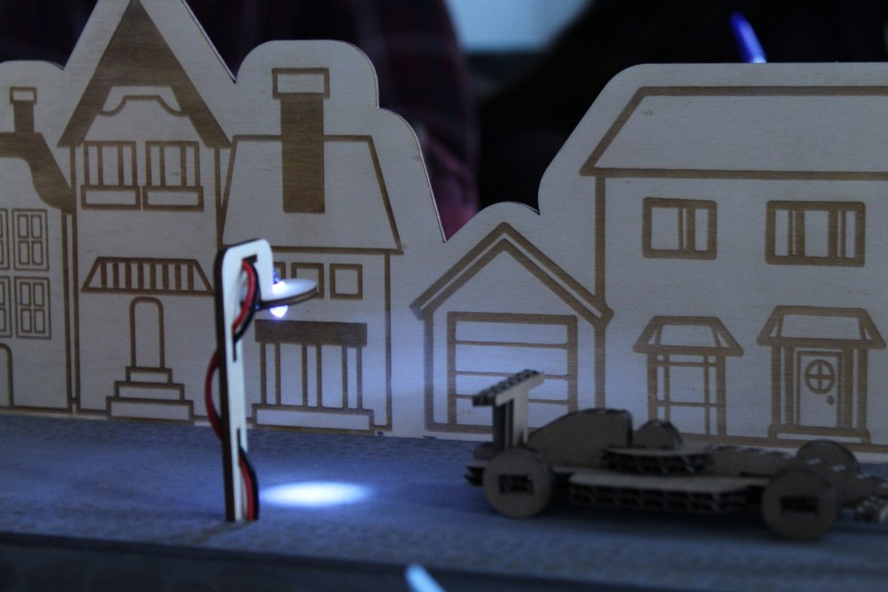 Häuserfassaden aus dem Lasercutter, davor eine Leuchte und ein Auto.