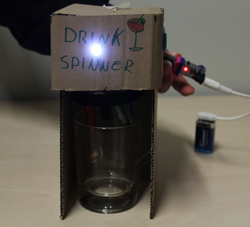Pappkonstruktion auf der &quot;Drink Spinner&quot; steht, daran eine Leuchte, darunter ein Glas.