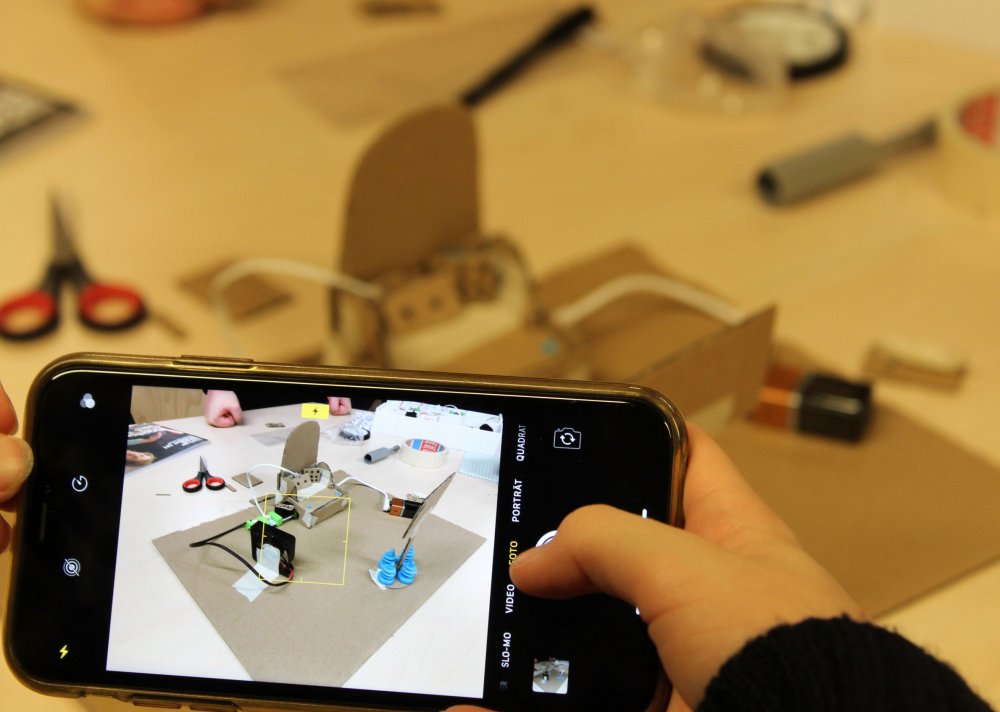 Tablet, dahinter verschwommen Tisch mit Schere, Pappen und ähnlichen Utensilien.