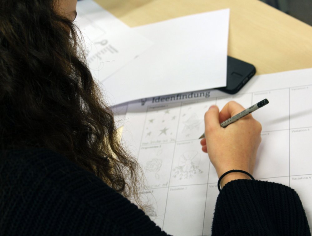 Junge Frau zeichnet Muster auf Papier.