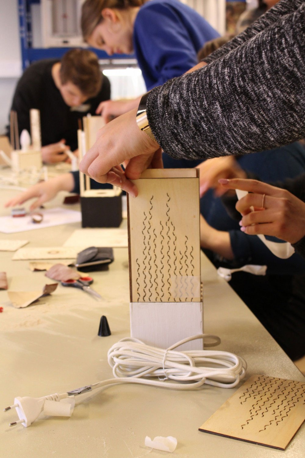 Menschen arbeiten mit Holzstücken an einem Tisch.