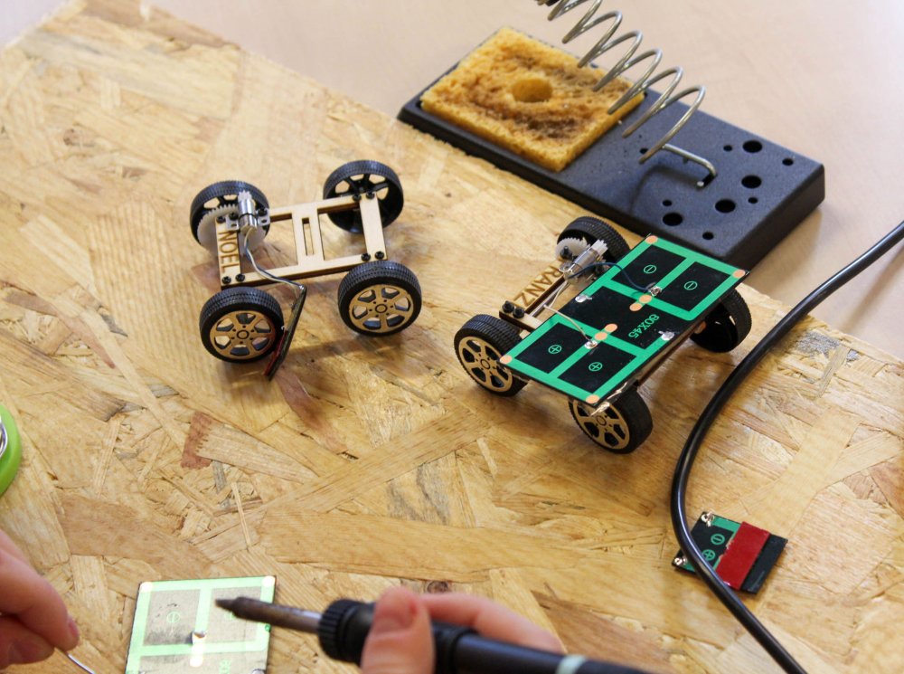 Bauteile des Solarautos und Hand mit Lötgerät.