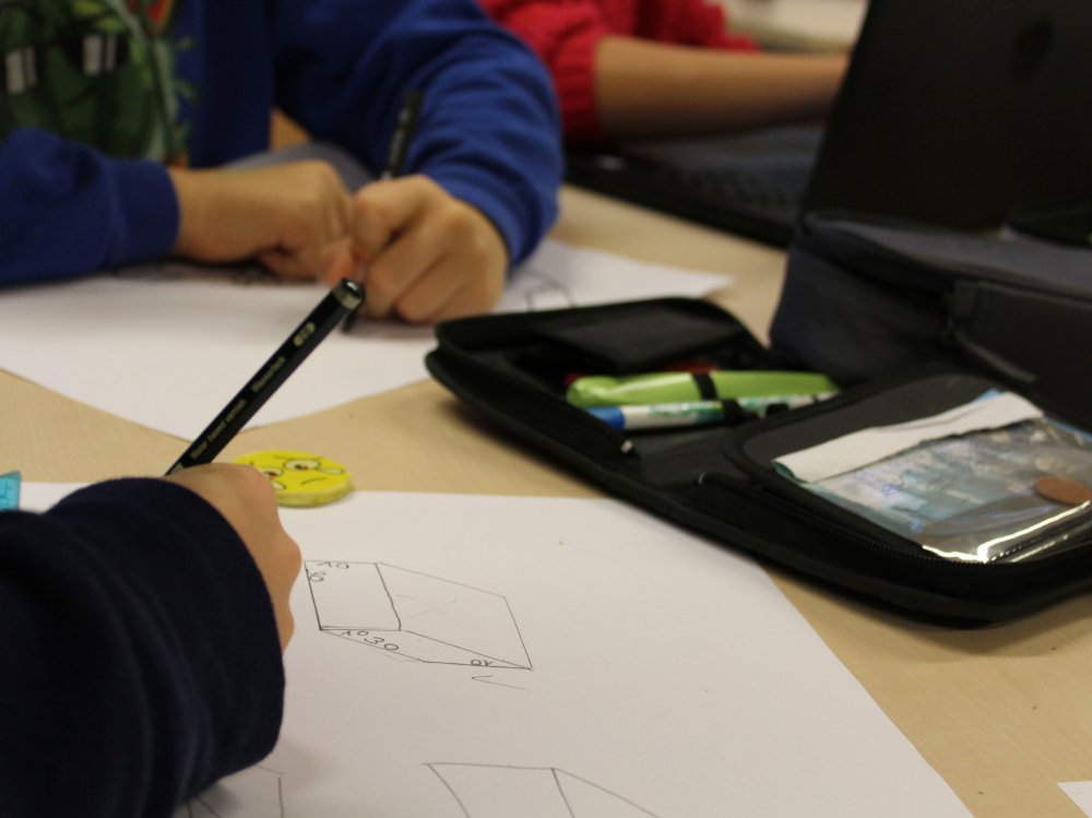 Papierblätter, Federmappe und Händde, die schreiben und skizzieren.