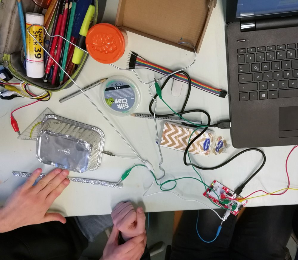 Draufsicht auf einen Tisch mit Laptop, Kabeln, Stiften, Klebstift und anderen Utensilien.