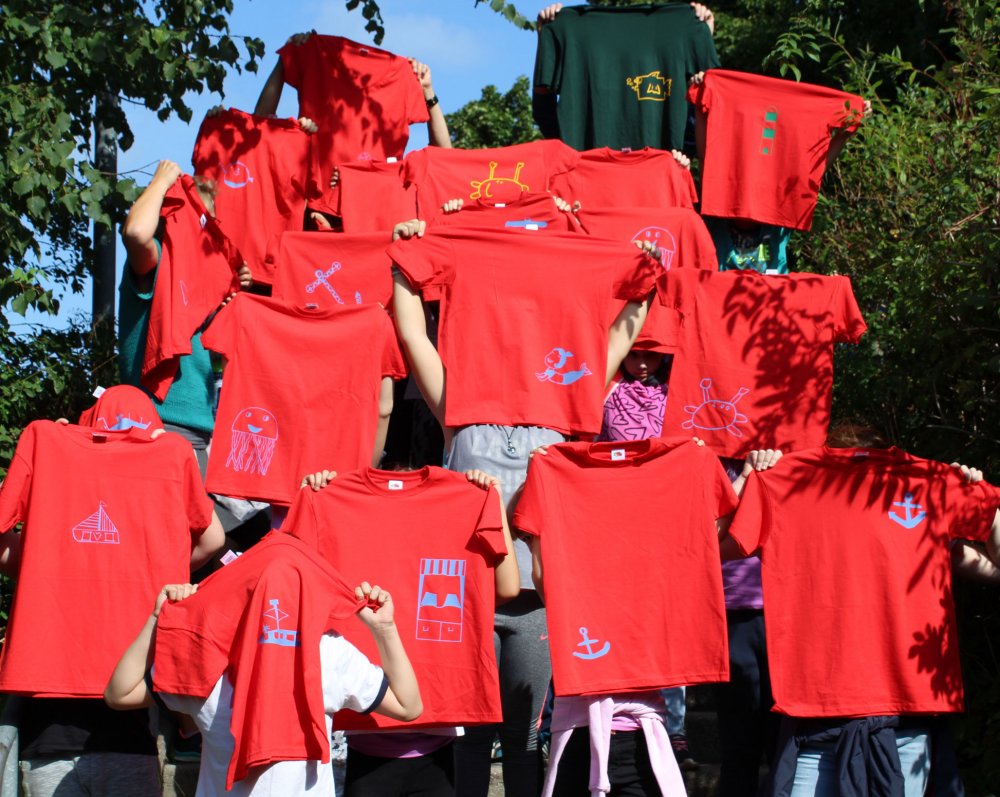 Menschen halten bedruckte T-Shirts in die Luft, die Gesichter sind nicht zu erkennen.