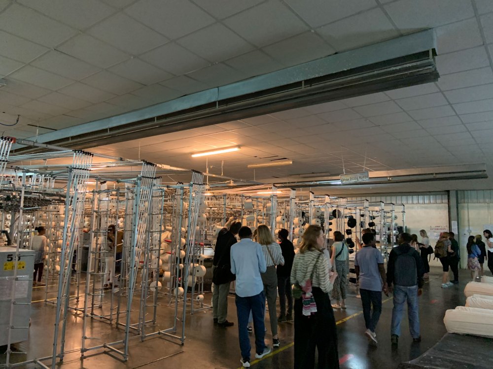 Menschengruppe in einer großen Halle mit Webmaschinen.