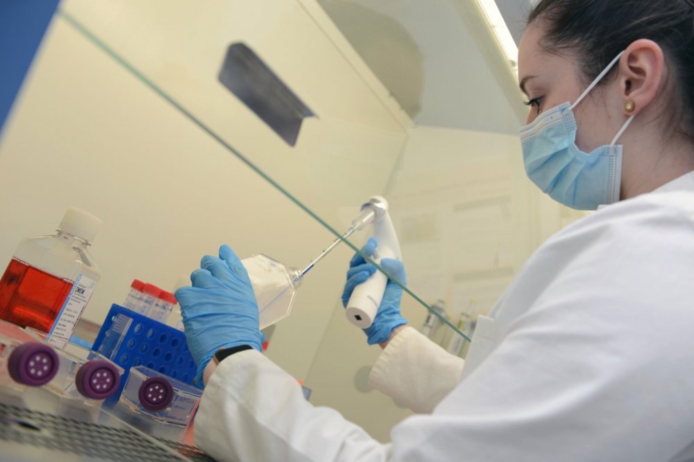 Studentin in Laborkittel und mit Handschuhen arbeitet an Proben.