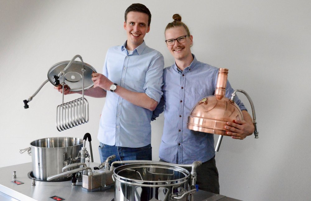 Zwei junge Männer posieren um den mobilen Brautisch. Sie halten Deckel für die Behälter im Tisch.