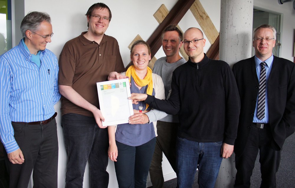 Gruppe aus Studierenden und Lehrenden posiert mit einer Urkunde.