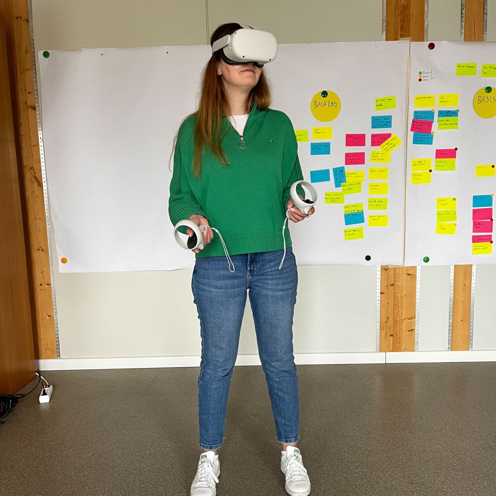 Eine junge Frau steht mit einer VR-Brille vor einer Wand mit Post-Its.