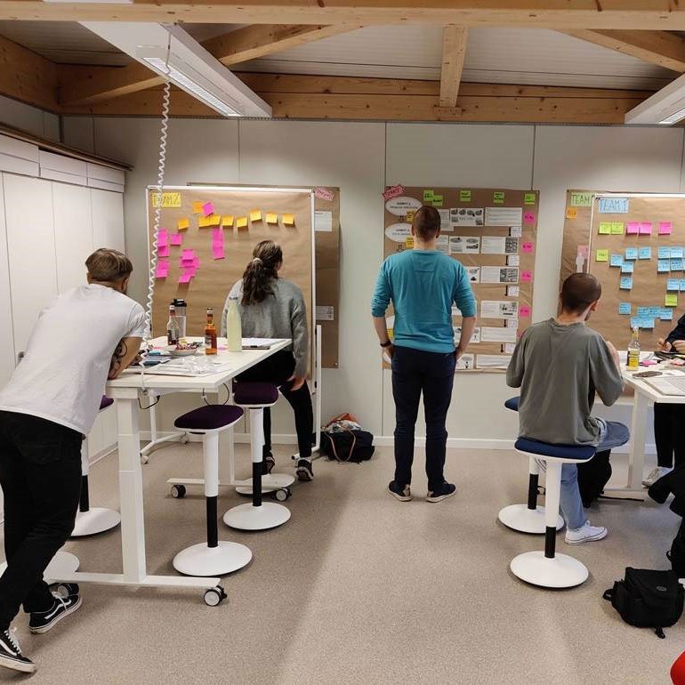 Junge Menschen an Tischen und vor Wänden  mit Post-Its.