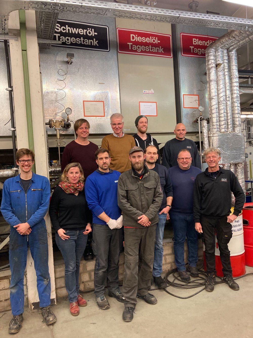 Gruppenbild: Etwa 10 Menschen posieren vor einer Anlage in einer Werkhalle. Sie tragen Arbeitskleidung.