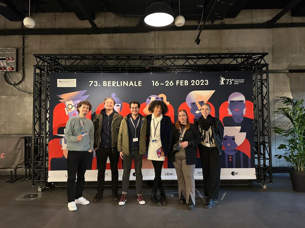 Kleine Gruppe junger Menschen steht vor einem Kino und lächelt in die Kamera.