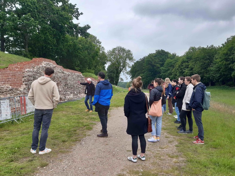 Gruppe von Menschen stehen auf und neben einem Sandweg. Neben ihnen ein Steinwall.