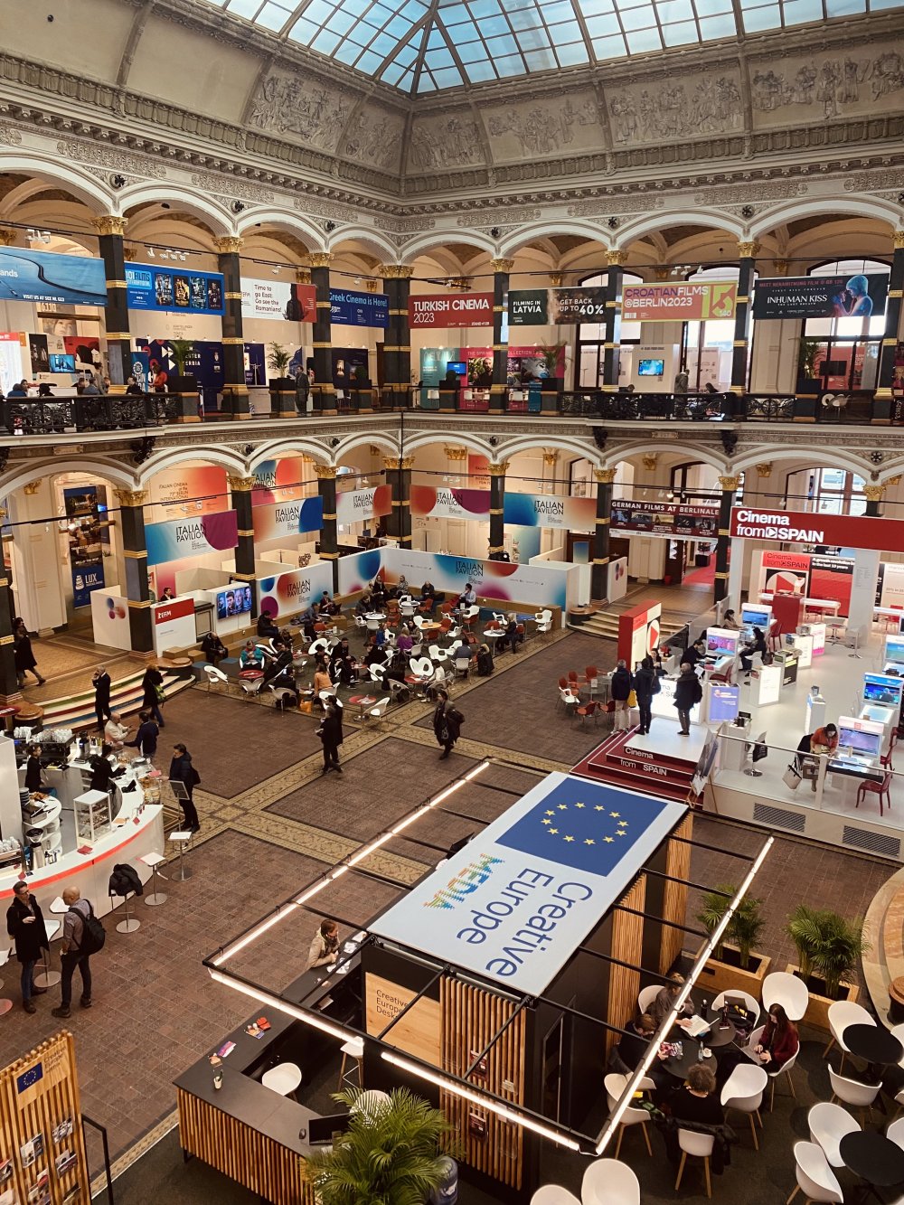Blick von oben auf eione Messehalle. Viele Stände und Menschen.