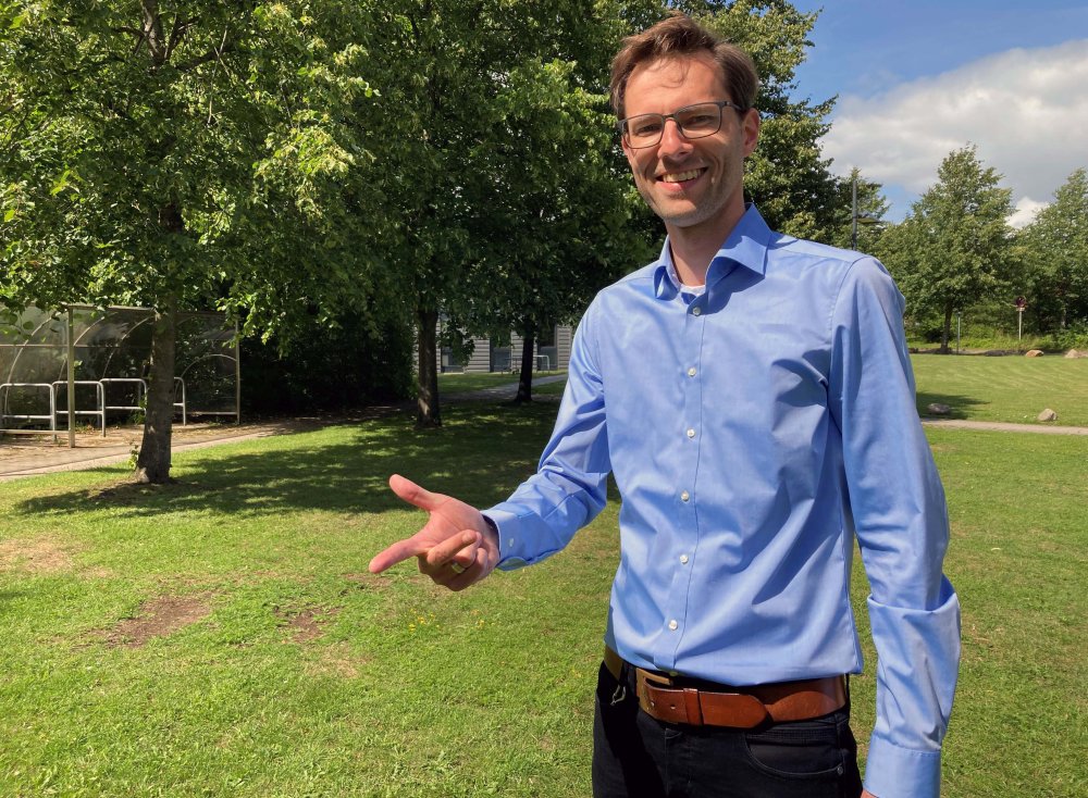 Dozent Alexander Voigt steht lächelnd auf einer Wiese auf dem Flensburger Campus.