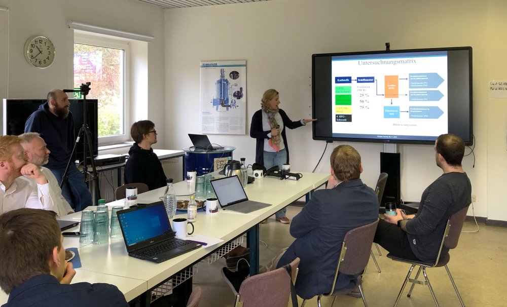 Seminarsituation: Eine Lehrende steht vor einer Gruppe und präsentiert etwas auf einem Bildschirm.