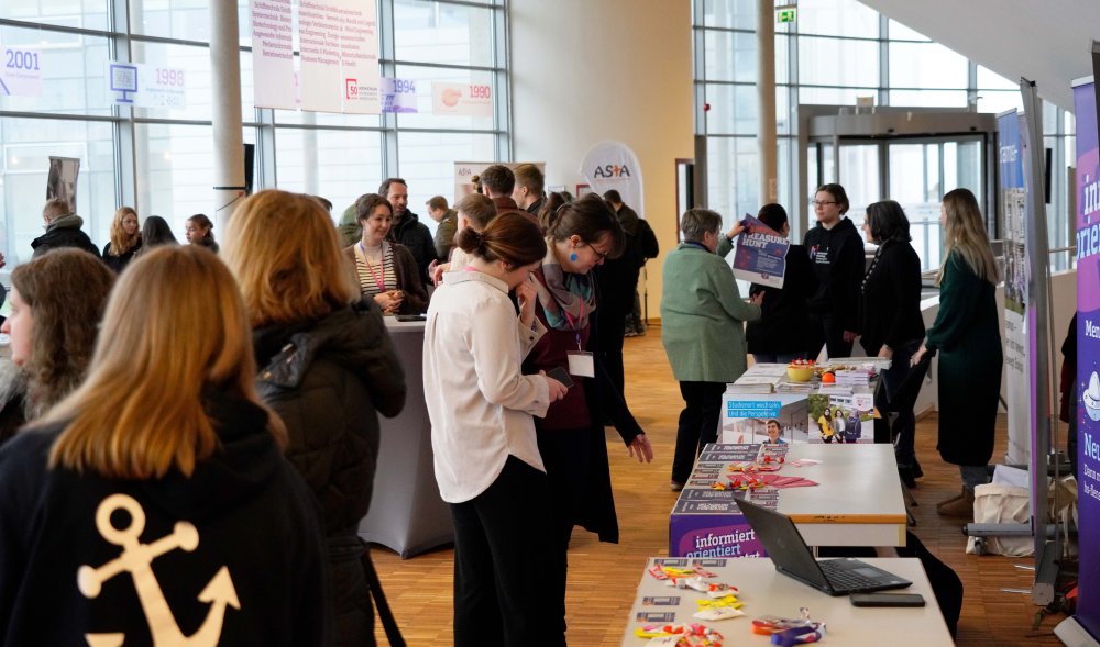 Viele Menschen stehen in einem Foyer und informieren sich an Info-Ständen und unterhalten sich. 