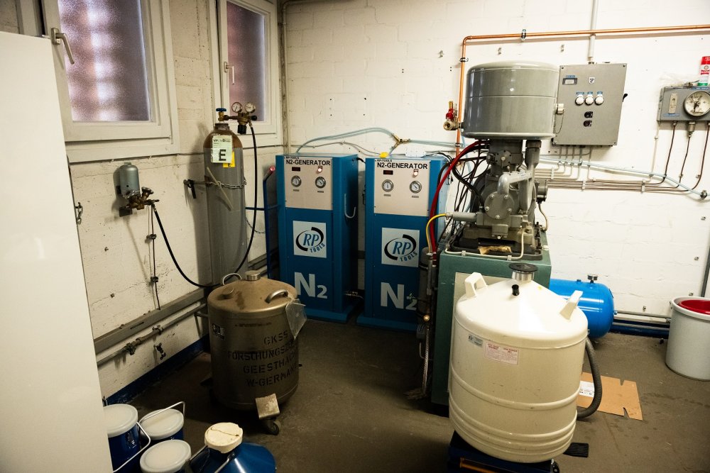 Eine technische Anlage: im Hintergrund zwei blaue Kästen, auf denen N2-Generator steht, davor eine Kühlanlage mit vielen Schläuchen und Verbindungen, im Vordergrund ein weißer Gastank.