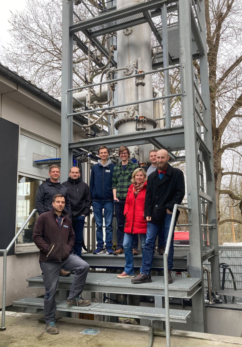 Gruppe von Menschen posiert auf einer Treppe, vor einer Turm-ähnlichen Konstruktion aus Metall.