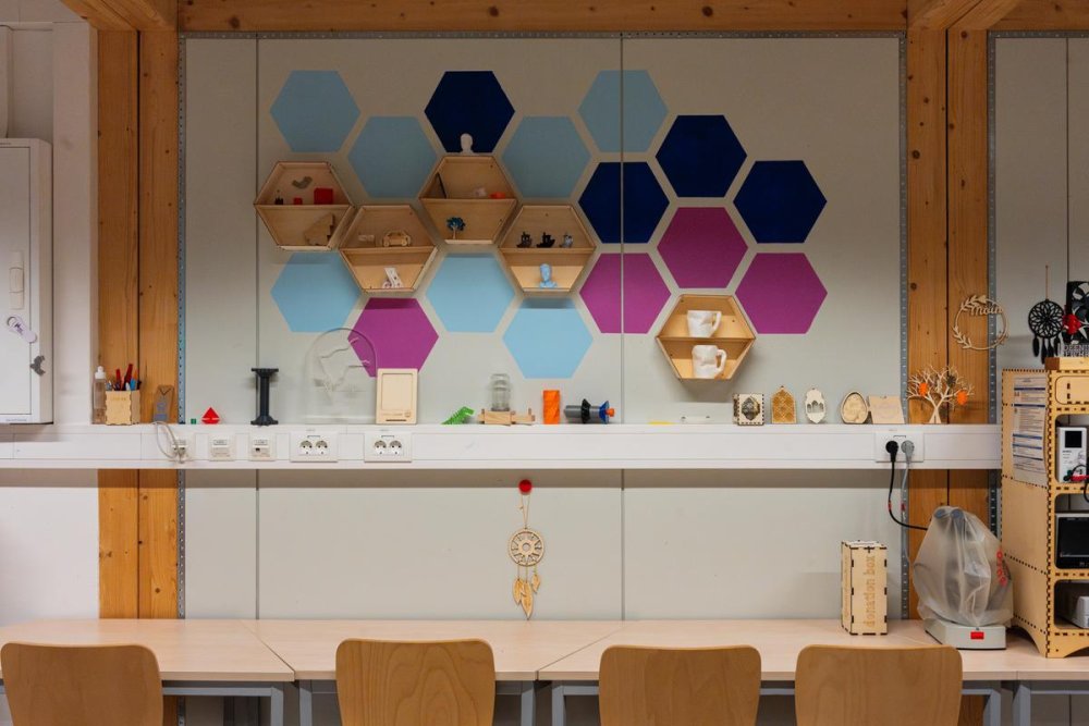 An einer Wand mit farbigen Sechsecken hängt ein Board mit verschiedenen selbstgemachten Dekoelementen, darunter ein Tisch mit Stühlen.