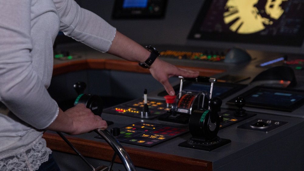 Nahaufnahme einer jungen Fraum, die ein Schiffs-Steuerrad in der einen Hand hält und mit der anderen einen Hebel nach vorn legt.