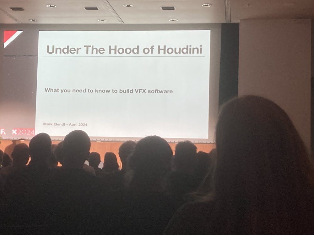 In einem dunklen Seminarsaal sieht man über die Köpfe des Publikums hinweg die Projektion einer Präsentationsfolie mit dem Text: "Under the Hood of Houdini - What you need to know to buildVFX software".