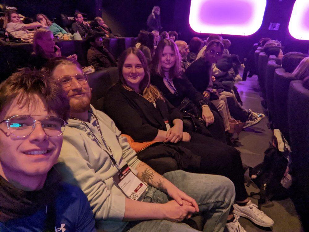 Eine Gruppe von Studierenden sitzt in einem dunklen Kinosaal und lächelt in die Kamera.