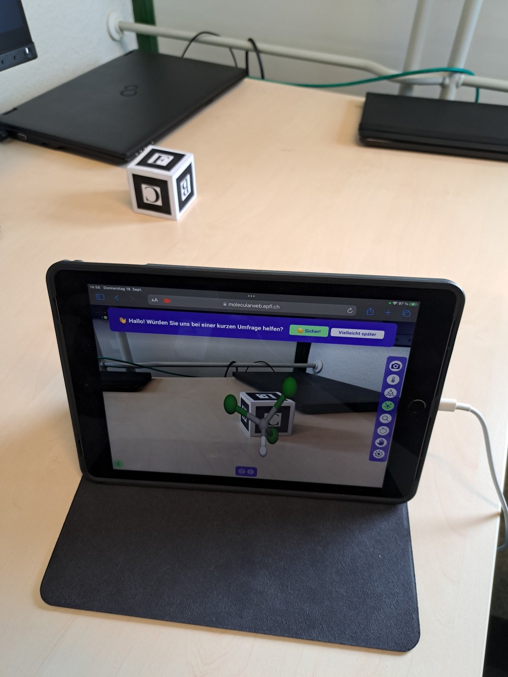 Auf einem Schreibtisch steht ein Tablet, auf dem ein virtuelles Modell eines Moleküls zu sehen ist.