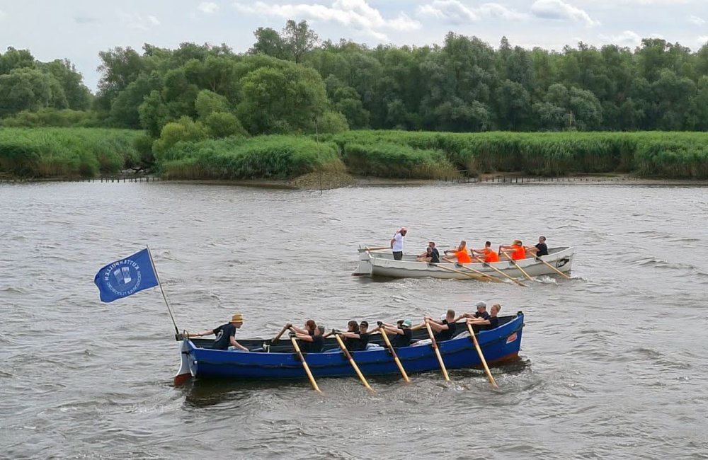 Auf einem Fluss rudern zwei Teams in breiten Kuttern um die Wette.