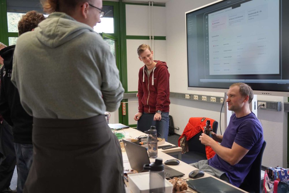 Um einen Tisch mit einer Menge miteinander verkabelten Sensoren sitzen und stehen eine Gruppe von Studierenden und unterhalten sich.