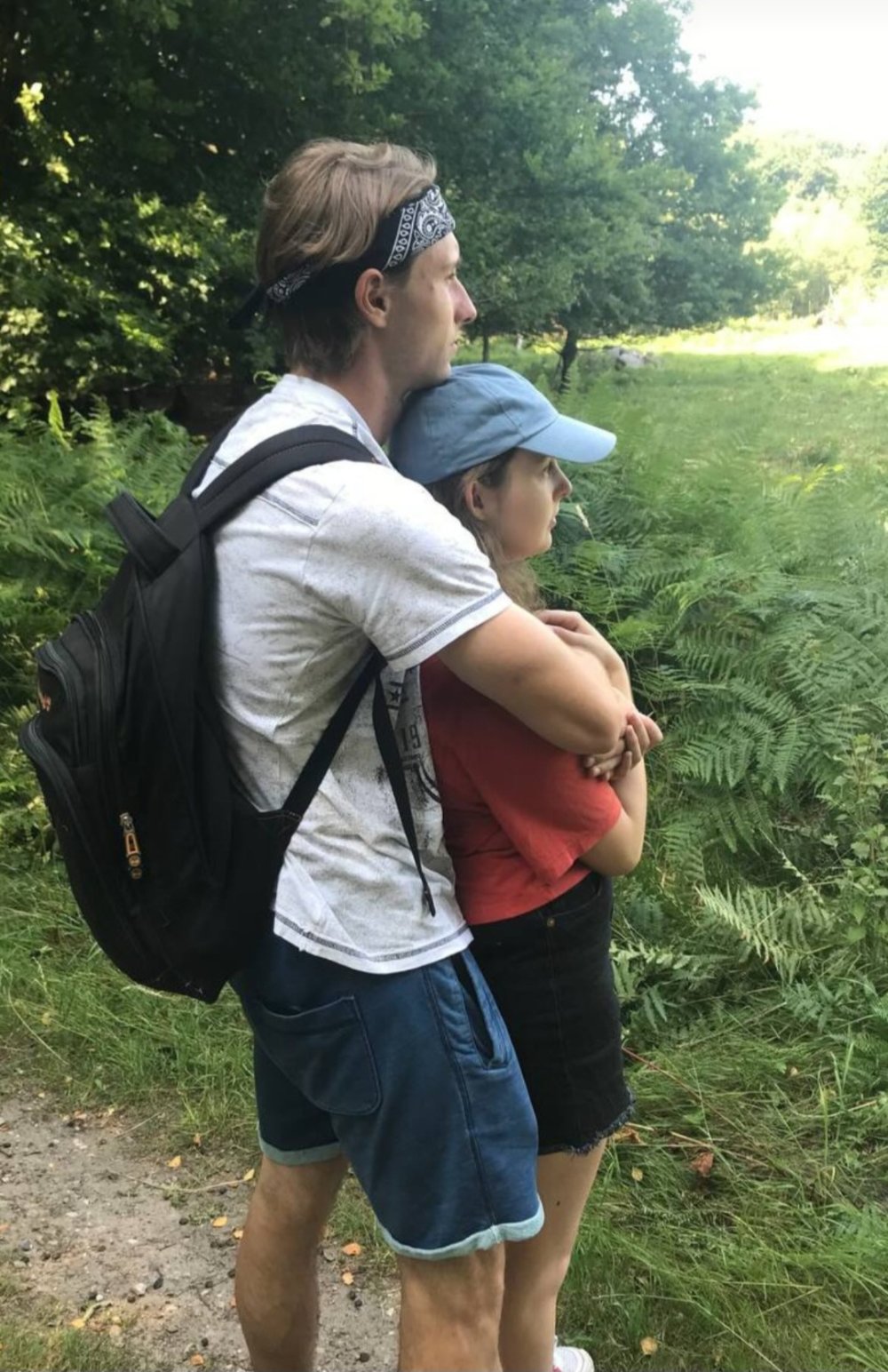 Ein junges Paar steht Arm in Arm auf einem Wanderweg und schaut in die Natur.