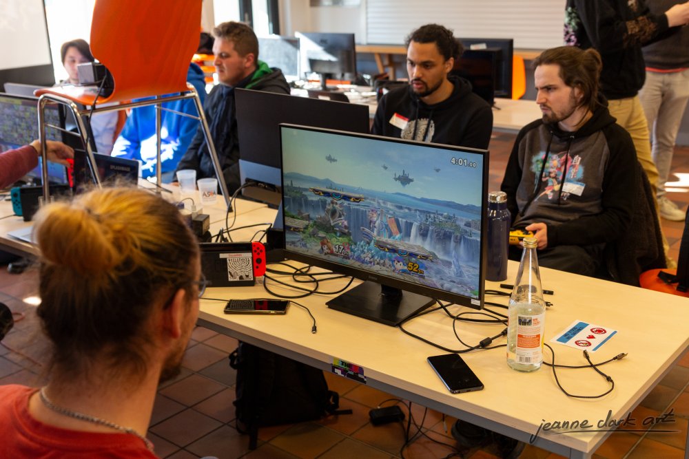 Vier junge Männer an einem Schreibtisch mit Monitor und Spielekonsole