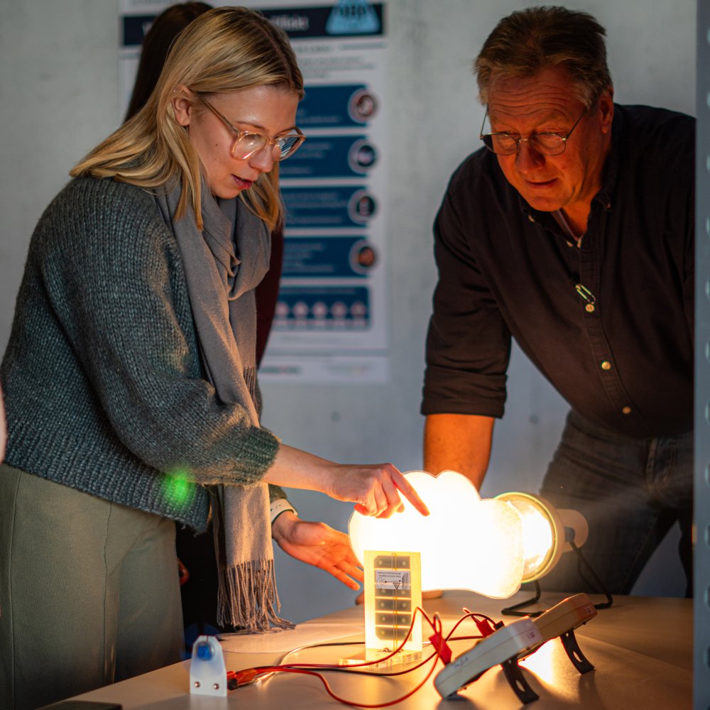 Eine Schülerin und ein Lehrer beugen sich über einen Wasserstoof-Versuchsaufbau.